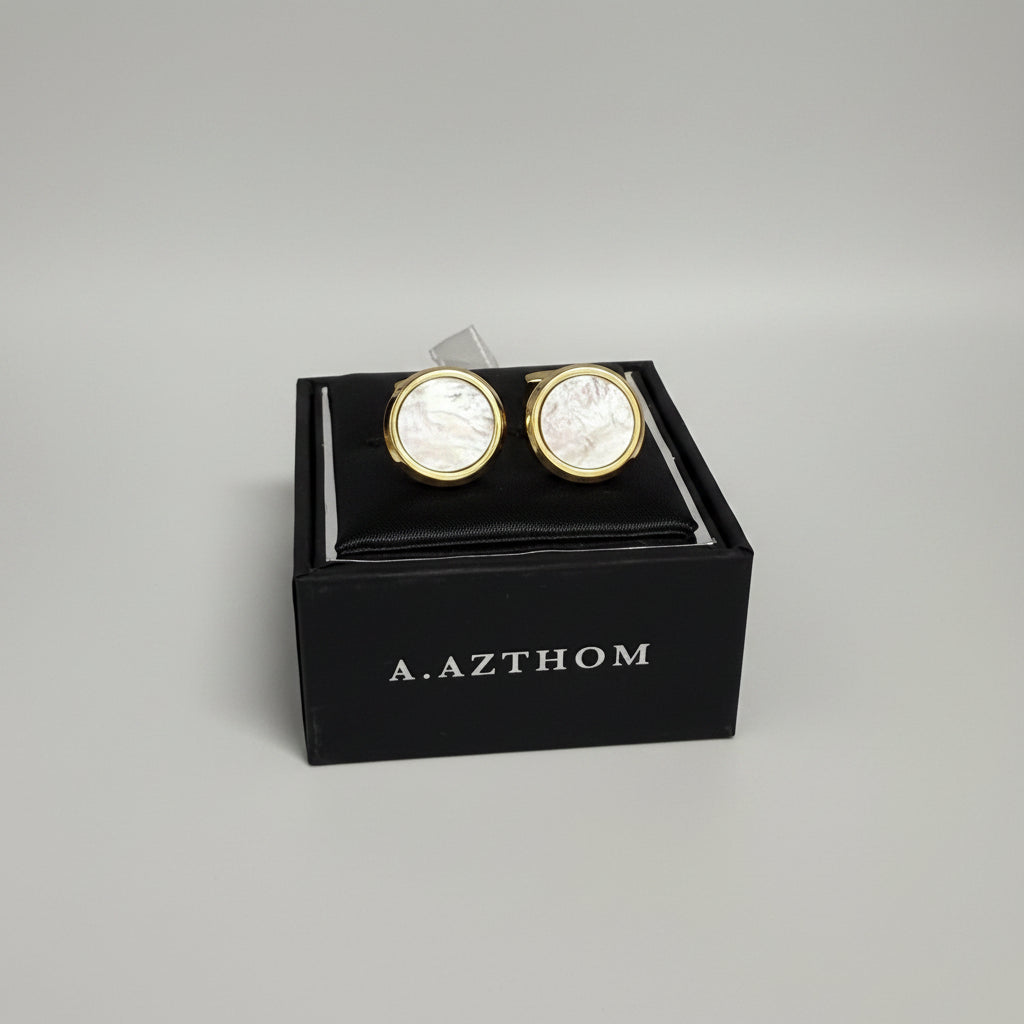 A pair of round gold cufflinks with iridescent mother-of-pearl faces, presented in a black A. Azthom gift box.