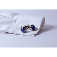 Pair of silver cufflinks with blue gemstones on a light gray background