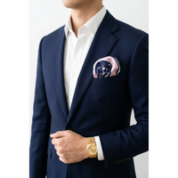 A man wearing a navy blue suit jacket, white dress shirt, and a pink pocket square with a dark blue pattern. He is also wearing a gold watch.